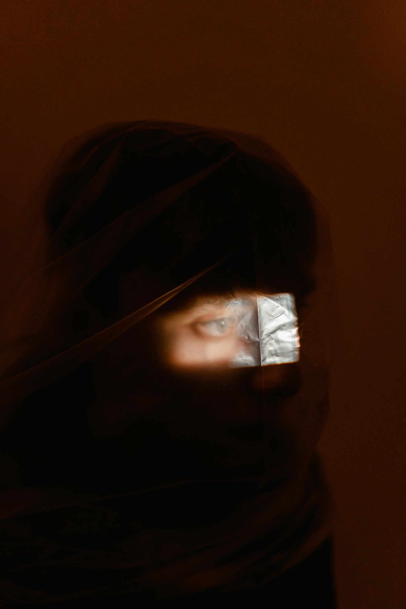 A mysterious and conceptual portrait featuring an eye through plastic wrap in a low light setting.